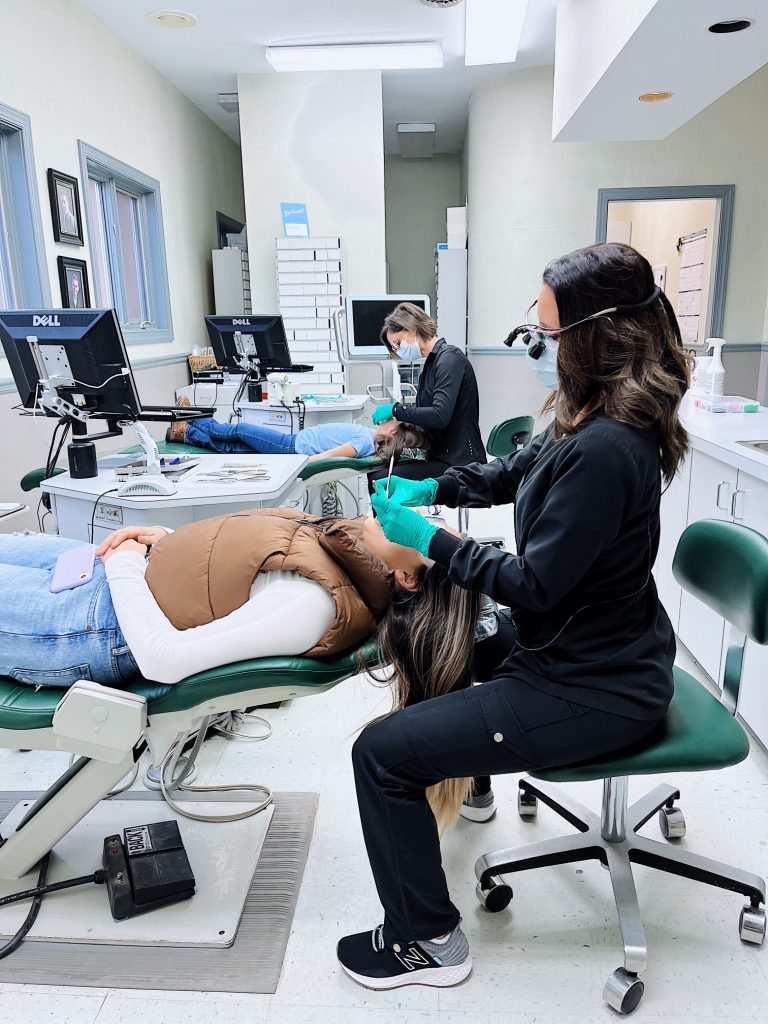 patient in dental chair with technician examining her mouth